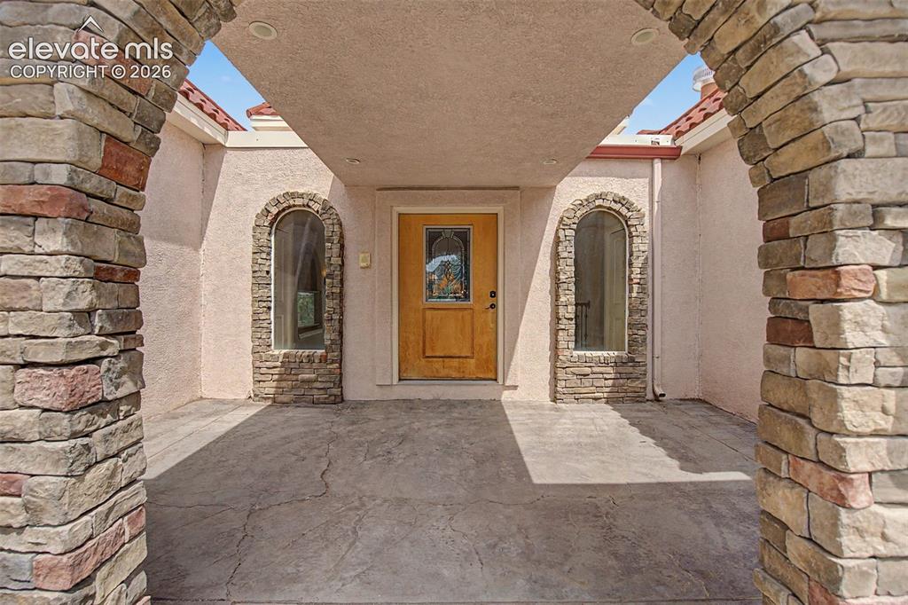 Image 4 of 50: Covered front entry with stone archways and custom wood door
