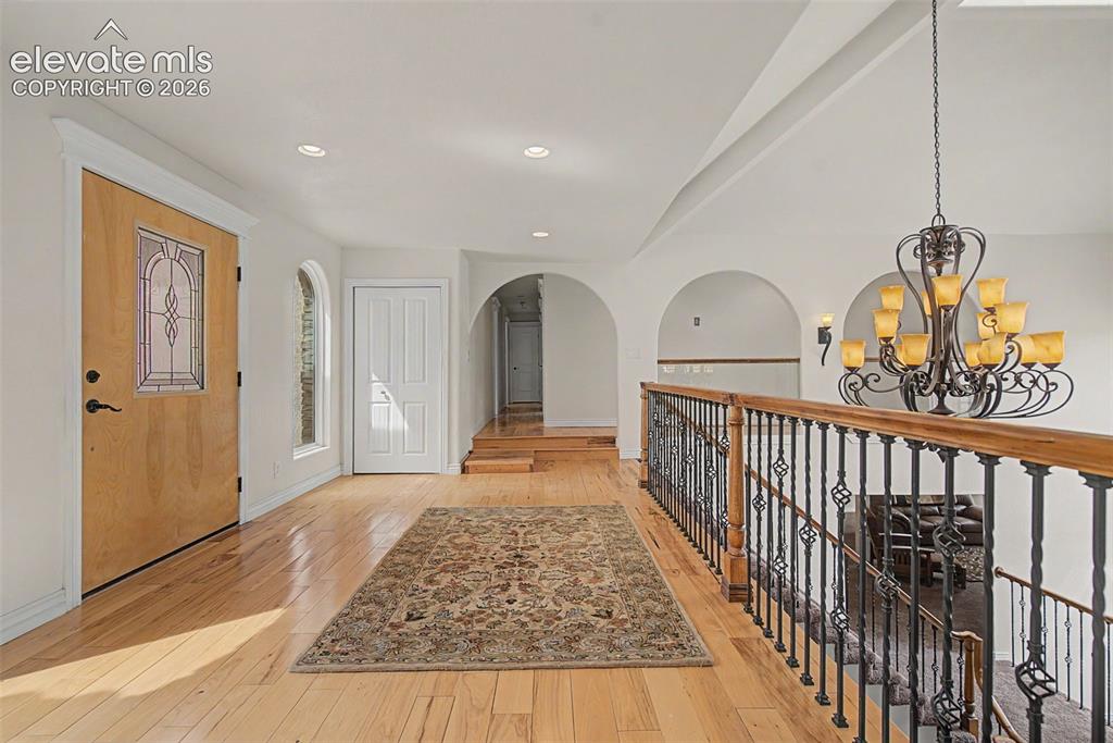 Image 5 of 50: Grand foyer with custom chandelier, wood flooring, and architectural arches