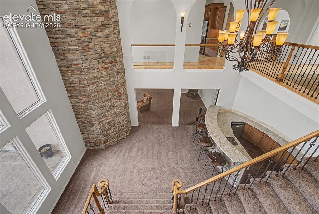 Image 9 of 50: Dramatic two-story foyer featuring a custom wet bar, stone accent wall, and