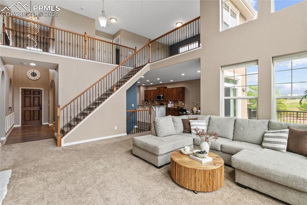 Image 3 of 36: Living room with a high ceiling, carpet flooring, stairs, and arched walkwa