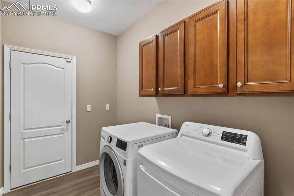 Image 32 of 36: Washroom with wood finished floors, washer and dryer, and cabinet space