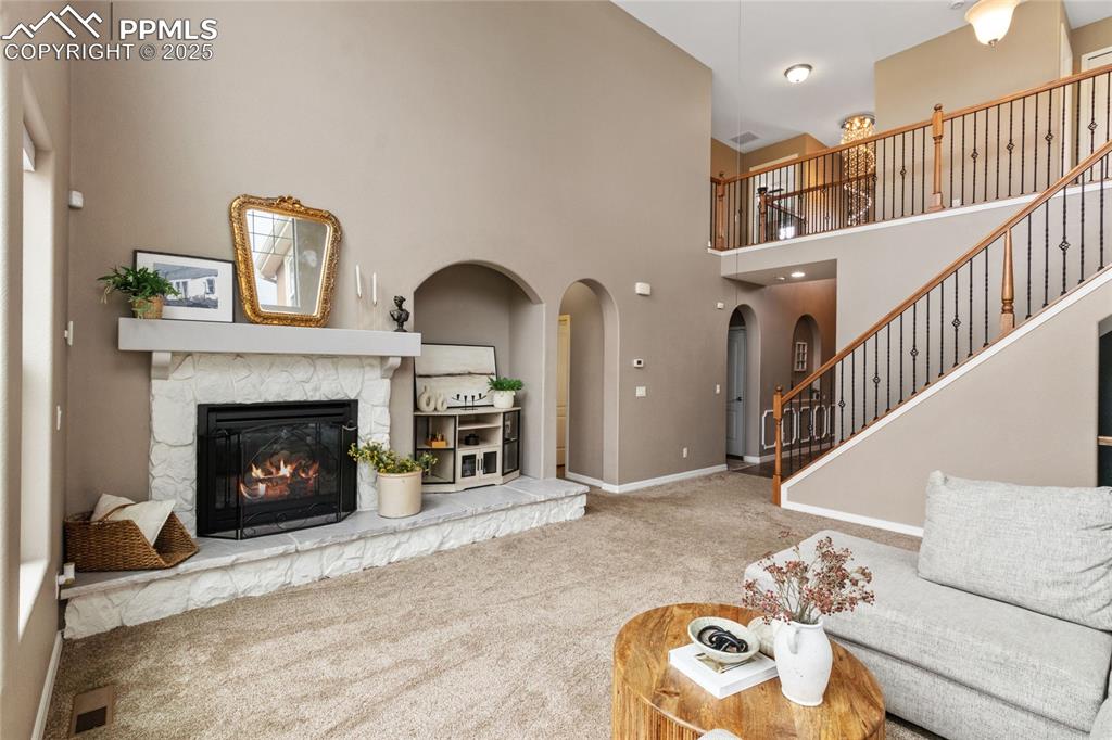 Image 5 of 36: Living room featuring carpet flooring, a high ceiling, a fireplace, arched 