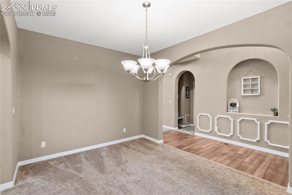 Image 6 of 36: Carpeted empty room with arched walkways and a chandelier