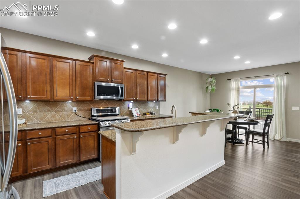Image 8 of 36: Kitchen featuring stainless steel appliances, a breakfast bar, dark wood-st