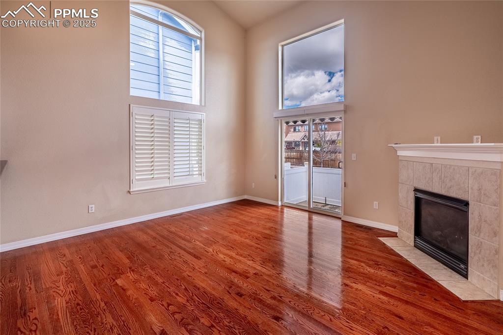 Image 12 of 47: Unfurnished living room featuring a high ceiling, a tiled fireplace, and wo