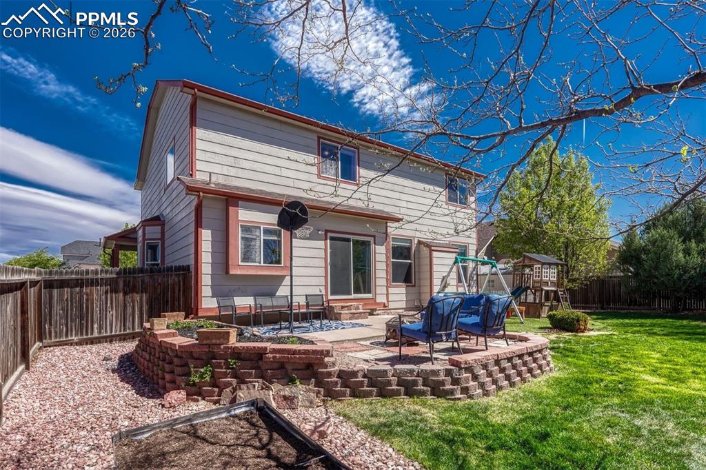 Image 37 of 40: Expansive backyard featuring a manicured lawn, a raised stone patio, and a 