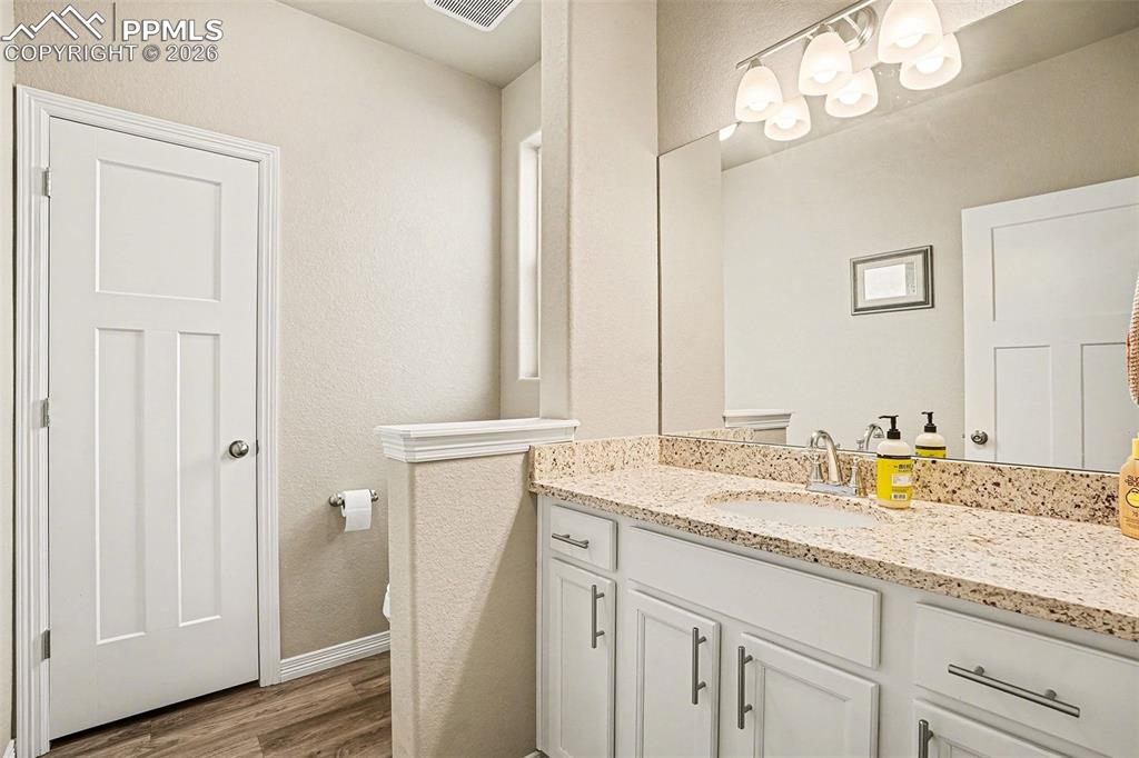 Image 12 of 35: Half bath with vanity, dark wood-style floors, and a textured wall