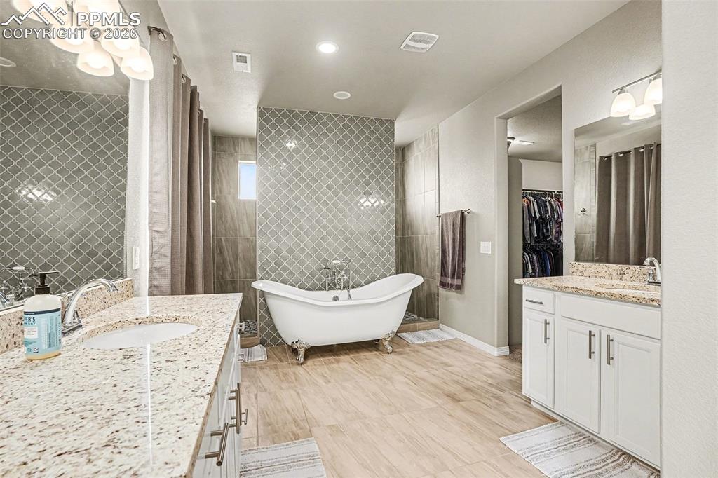 Image 13 of 35: Bathroom featuring two vanities, a walk in closet, a soaking tub, tile wall