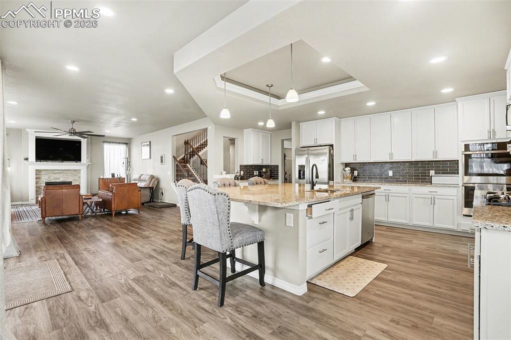 Image 5 of 35: Kitchen featuring white cabinets, a tray ceiling, a breakfast bar, light st