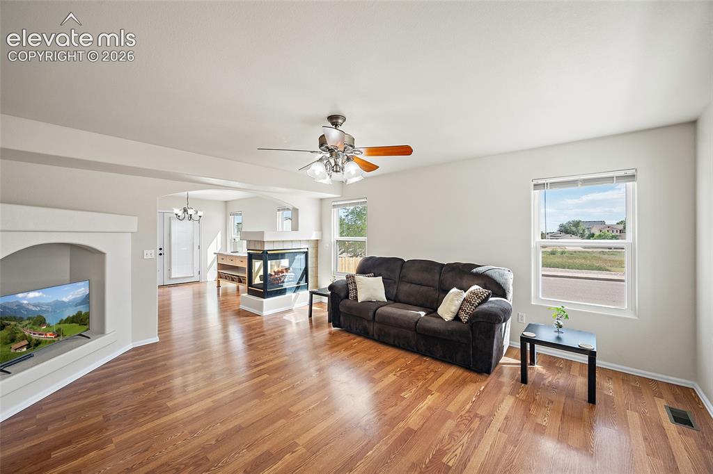 Image 10 of 41: Open living area with hardwood floors, large windows, and a three-sided fir