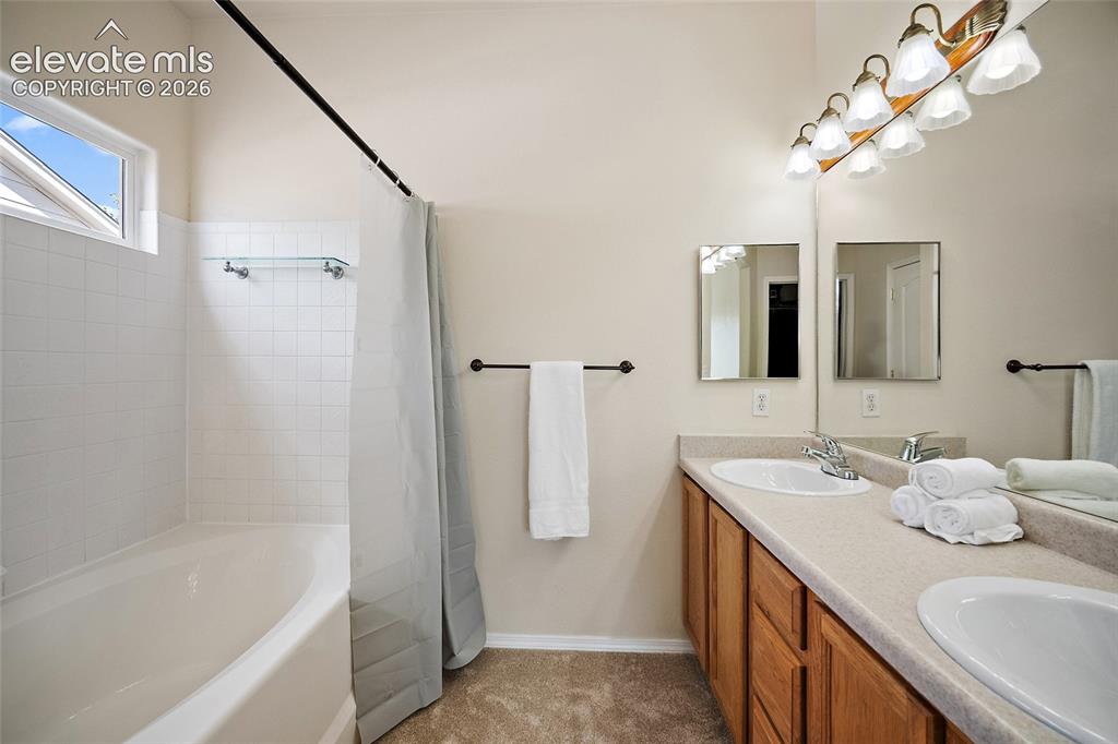 Image 14 of 41: Primary bathroom with double-sink vanity, tiled tub and shower surround, ge