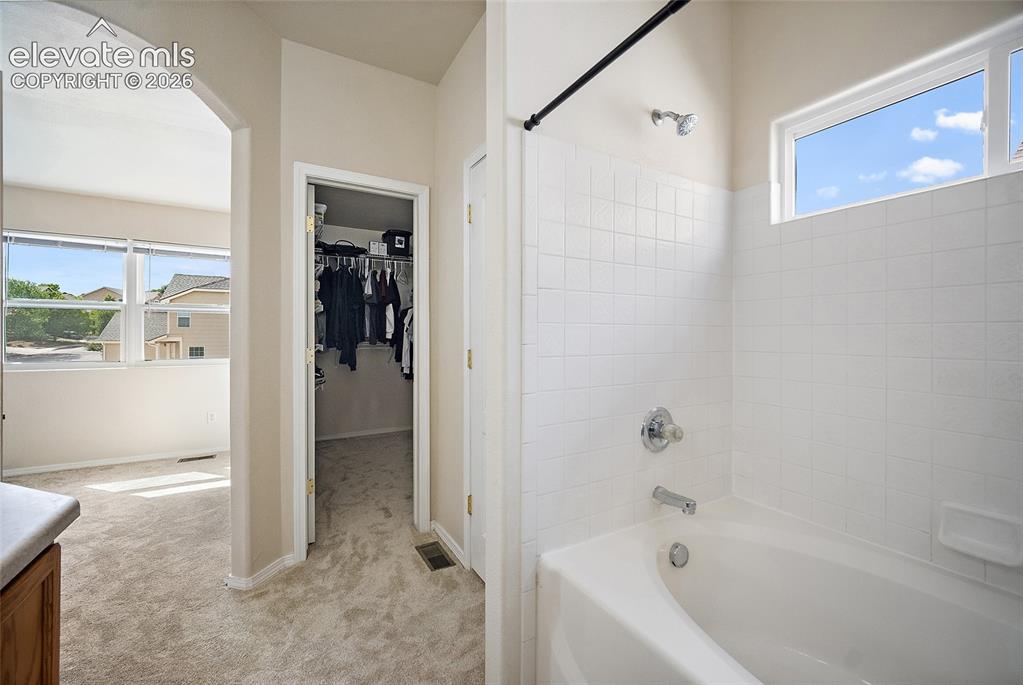 Image 15 of 41: Primary bath featuring a tiled tub and shower area, large window, and conve