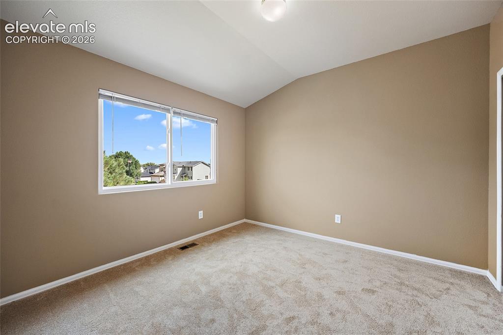 Image 22 of 41: Secondary bedroom with vaulted ceiling, large window, soft carpeting, and f