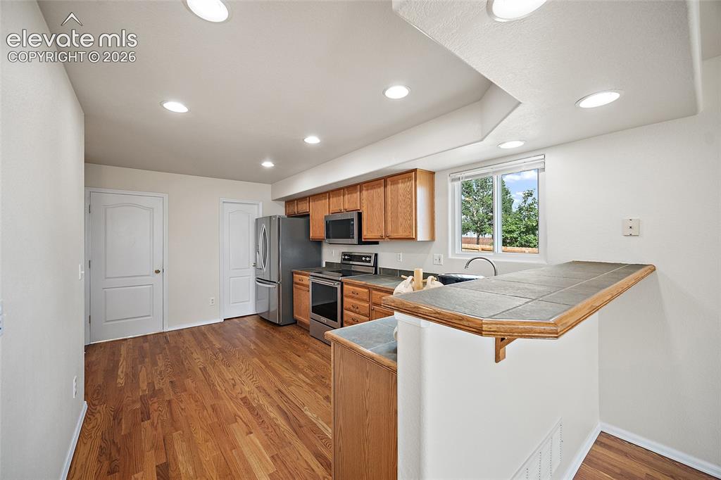 Image 7 of 41: Bright kitchen with hardwood flooring, oak cabinetry, stainless steel appli