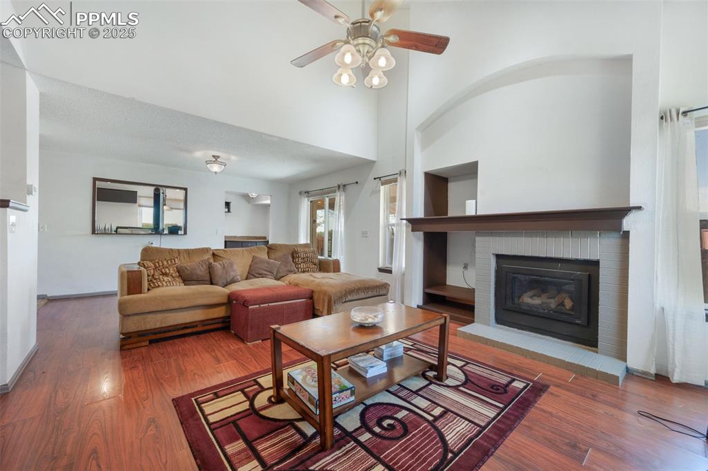 Image 12 of 50: Living room featuring a brick fireplace, wood finished floors, a ceiling fa