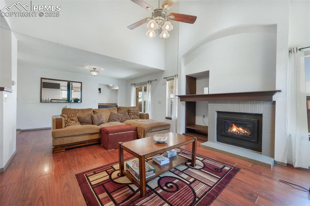 Image 13 of 50: Living area featuring a brick fireplace, wood finished floors, a high ceili
