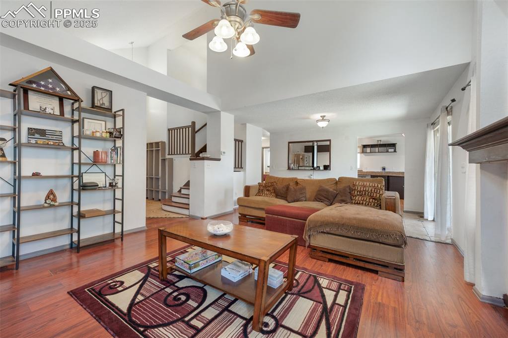 Image 14 of 50: Living room with ceiling fan, stairs, wood finished floors, and high vaulte