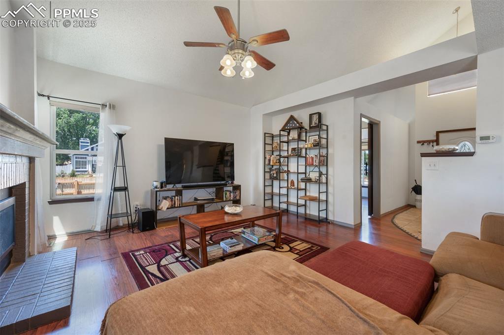 Image 15 of 50: Living area with a ceiling fan, a fireplace, and wood finished floors