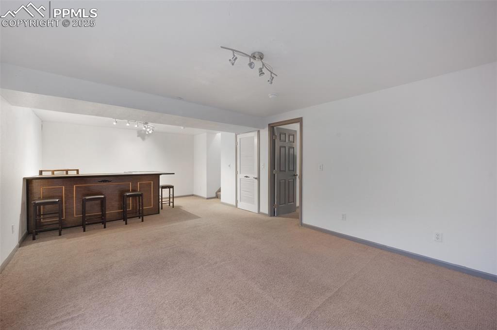 Image 32 of 50: Living room with a dry bar, light carpet, and rail lighting