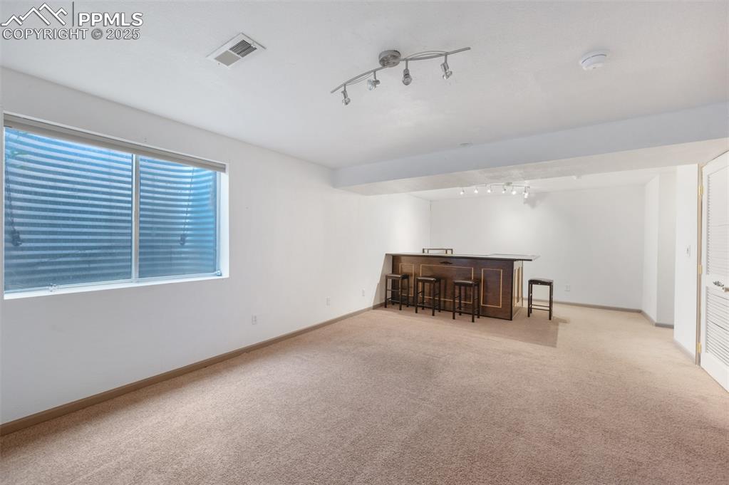 Image 33 of 50: Unfurnished room featuring rail lighting, bar, and carpet floors