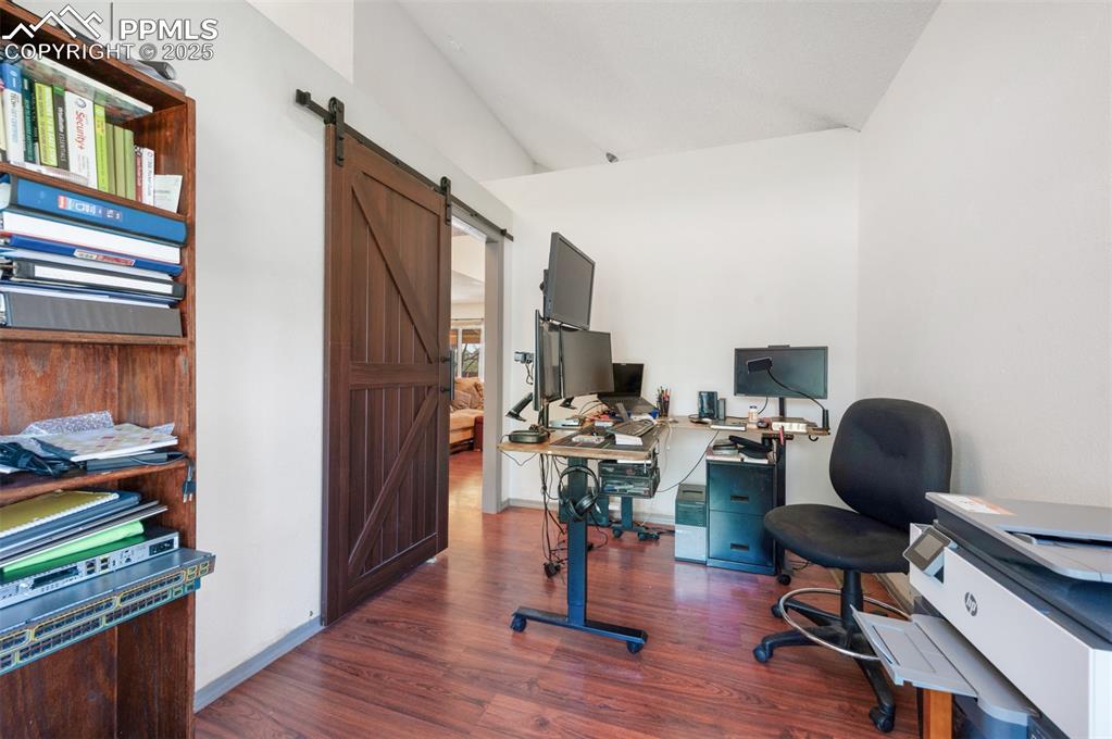 Image 9 of 50: Office featuring lofted ceiling, a barn door, and dark wood finished floors