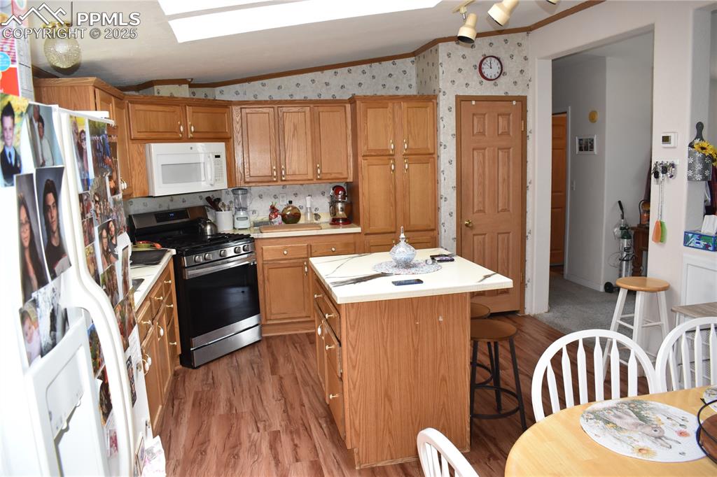 Image 28 of 47: Kitchen with vaulted ceiling, white appliances, light countertops, brown ca