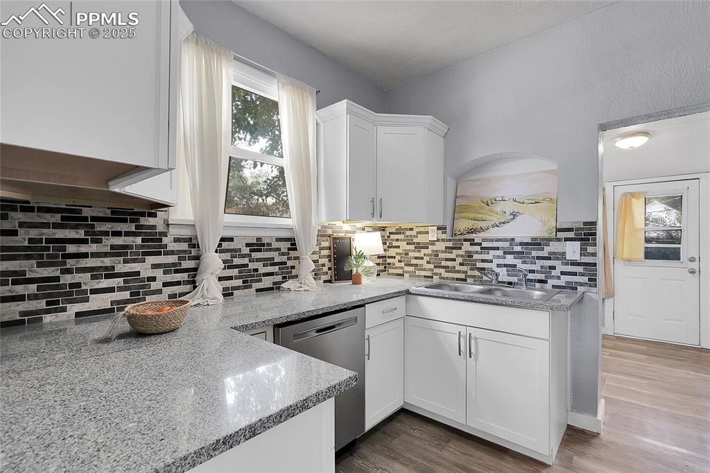 Image 17 of 29: Kitchen featuring white cabinets, dishwasher, wood finished floors, light s