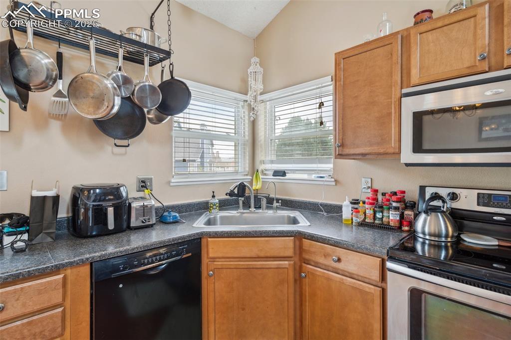 Image 15 of 35: Kitchen featuring brown cabinets, stainless steel appliances, dark countert