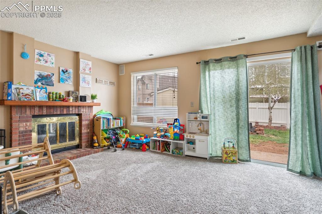 Image 17 of 35: Rec room with a brick fireplace, a textured ceiling, visible vents, and car