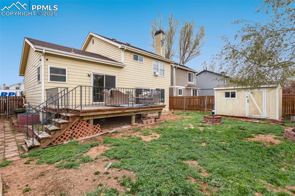 Image 34 of 35: Back of property with a fenced backyard, a fire pit, a deck, and a storage