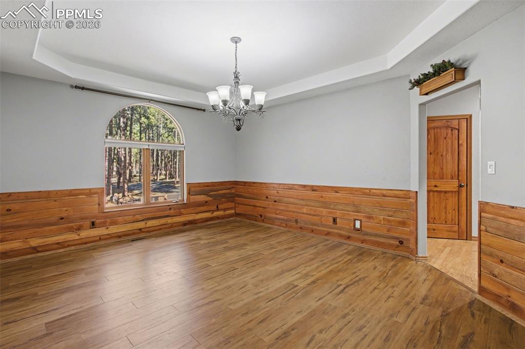 Image 10 of 50: Spare room featuring a tray ceiling, wainscoting, a chandelier, wooden wall