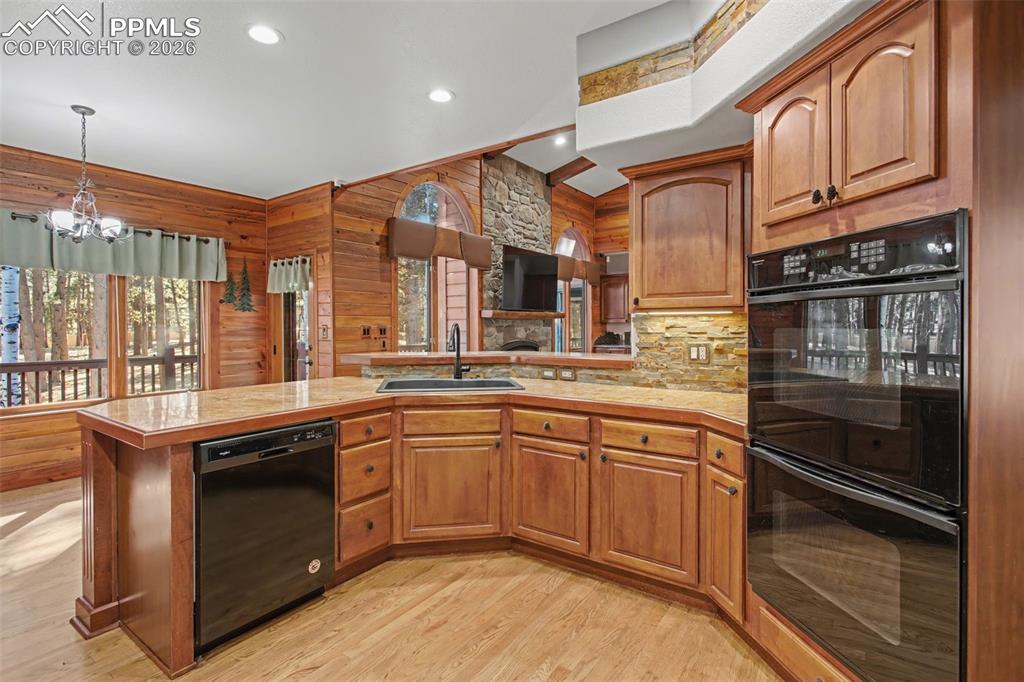 Image 17 of 50: Kitchen featuring black appliances, a peninsula, light countertops, wood fi
