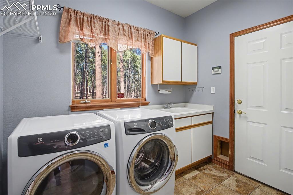 Image 23 of 50: Laundry area featuring separate washer and dryer, cabinet space, and stone 