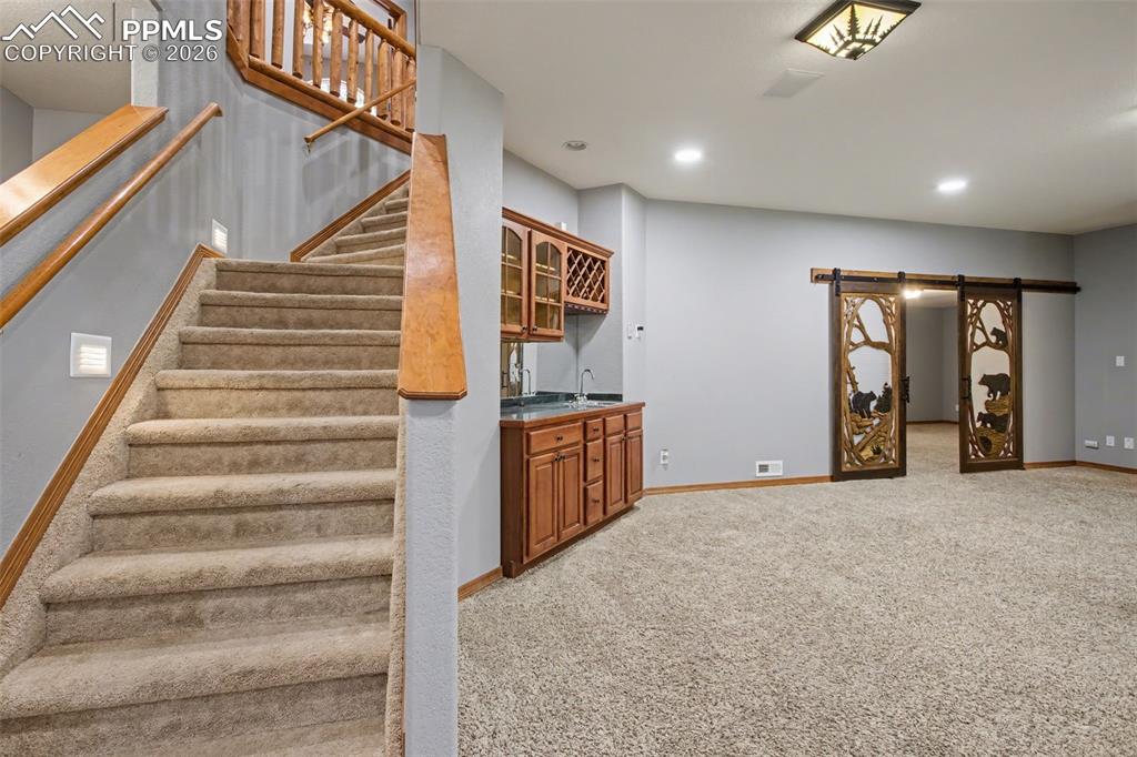 Image 28 of 50: Stairs featuring carpet, wet bar, a barn door, and recessed lighting