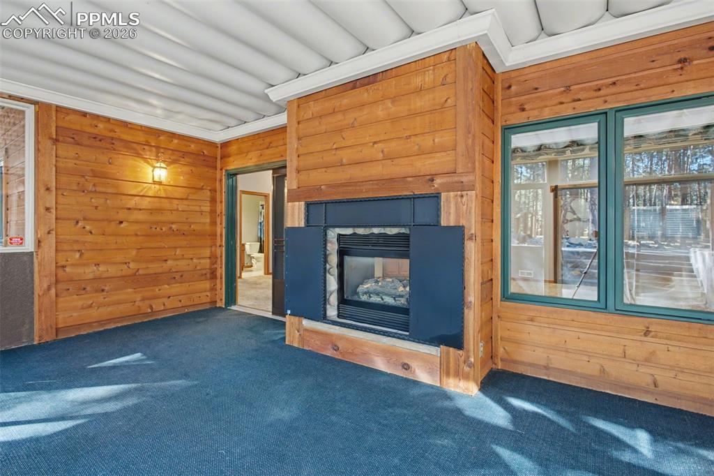Image 41 of 50: Unfurnished living room with wooden walls, carpet, and a stone fireplace
