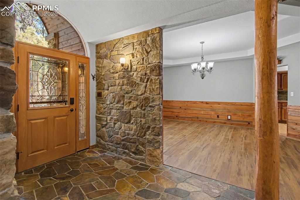 Image 8 of 50: Entrance foyer with wooden walls, stone flooring, wainscoting, and a chande