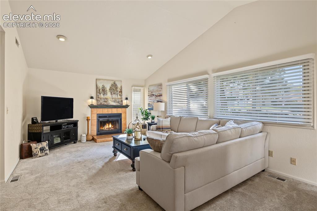 Image 13 of 27: Vaulted ceiling, recessed lighting, gas fireplace with tile surround, carpe