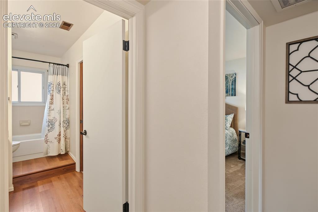 Image 18 of 27: Wood-finish flooring leading to a full bathroom with a white tub and a wind
