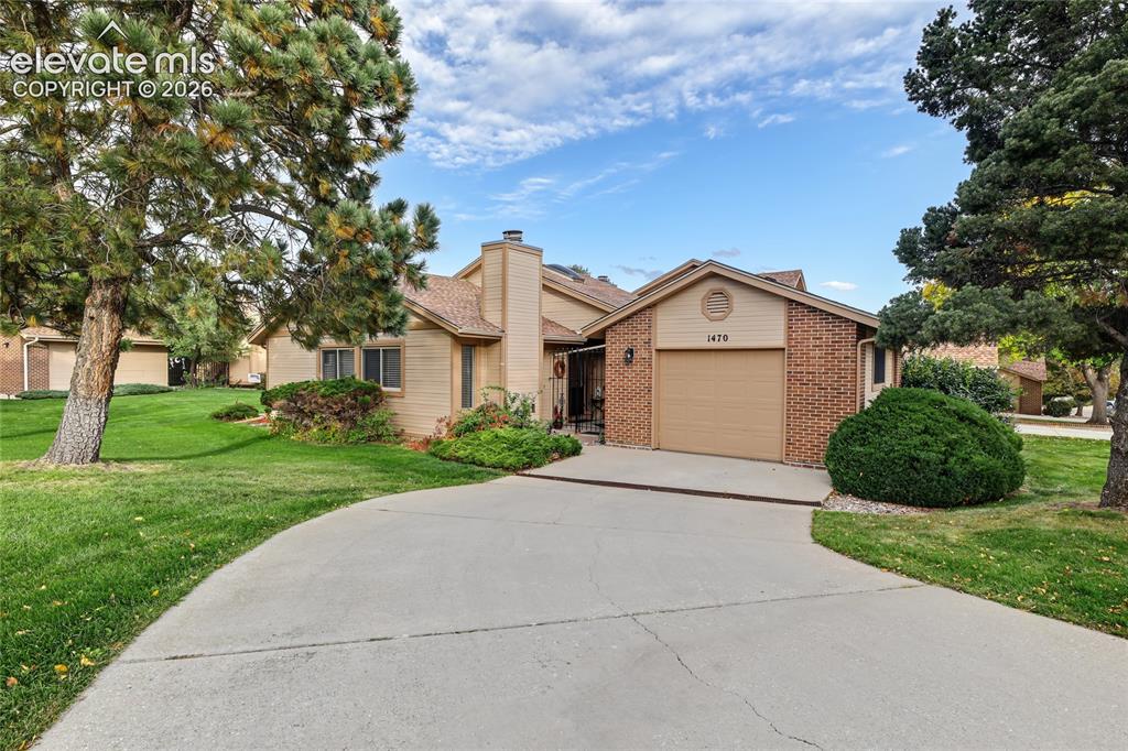 Image 2 of 27: Brick and siding exterior with an attached garage, paved driveway, and matu