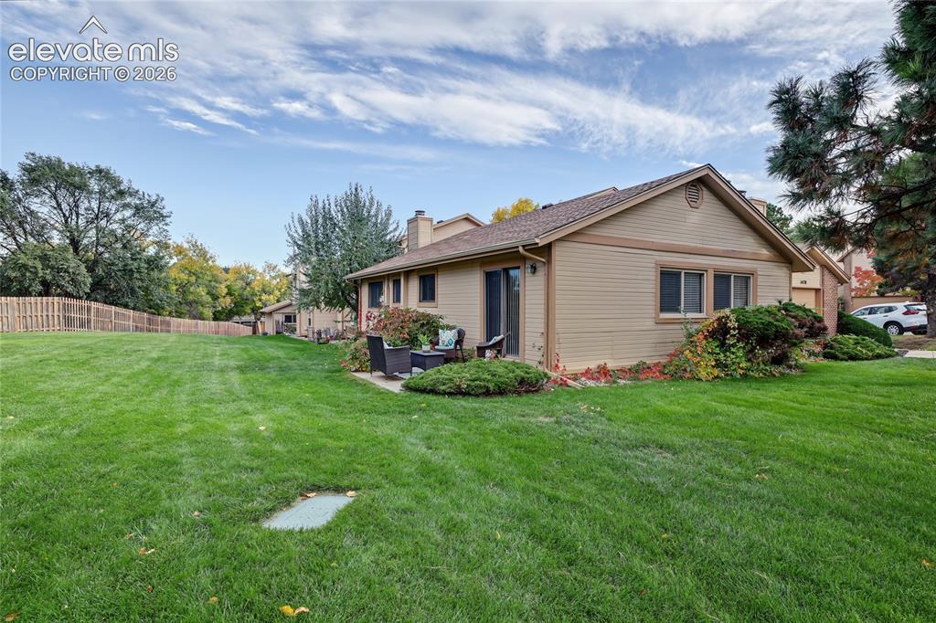 Image 25 of 27: Expansive grass yard with wood fencing, mature trees, a side patio, and a s