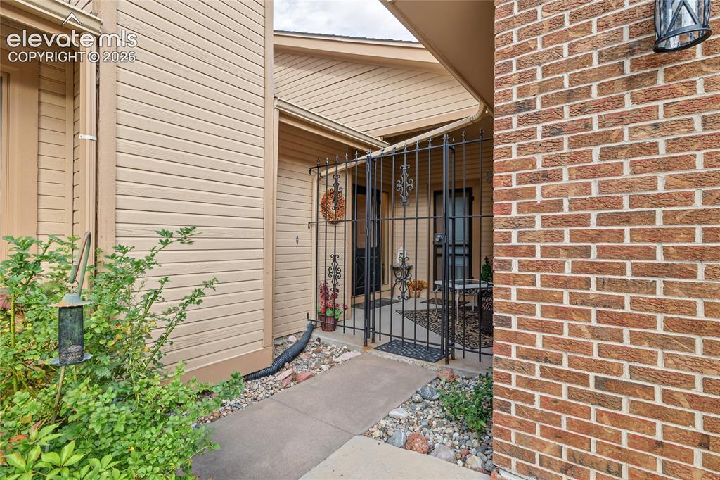 Image 3 of 27: Brick exterior with siding accents, secure wrought iron gate, and concrete 