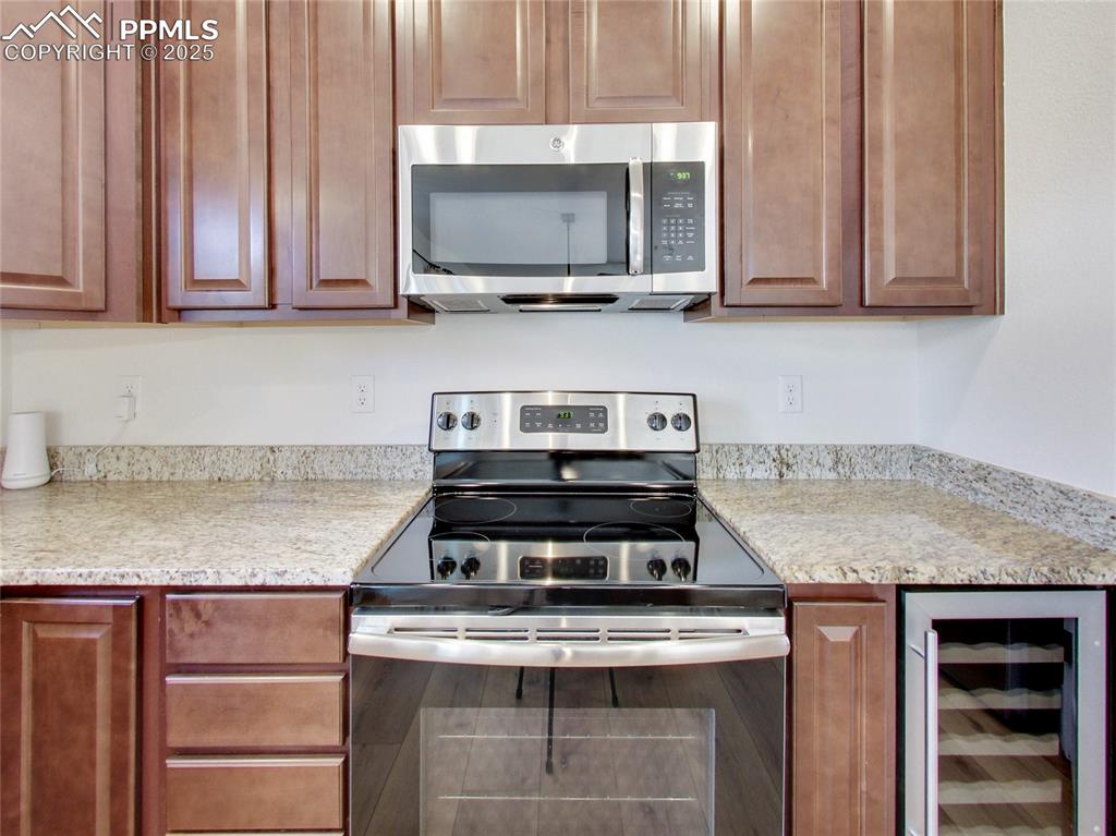 Image 13 of 37: Kitchen with stainless steel appliances, wine cooler, and light stone count