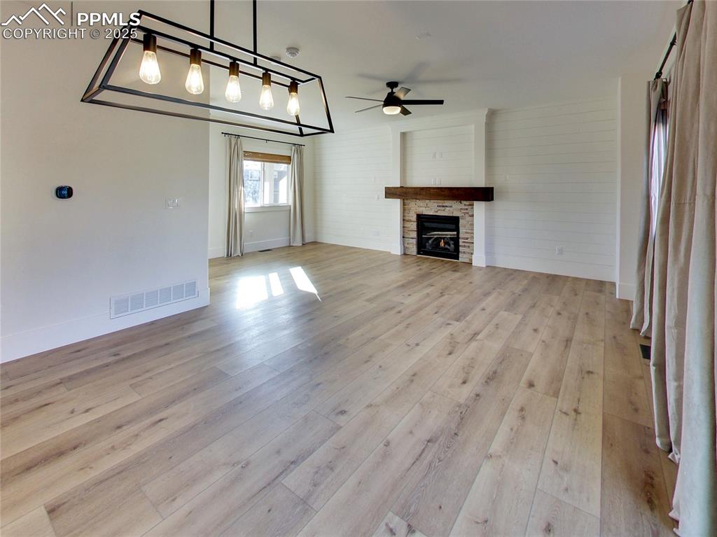 Image 16 of 37: Unfurnished living room with ceiling fan, a stone fireplace, and light wood