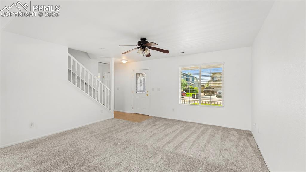 Image 7 of 46: Unfurnished living room with carpet, stairs, and ceiling fan