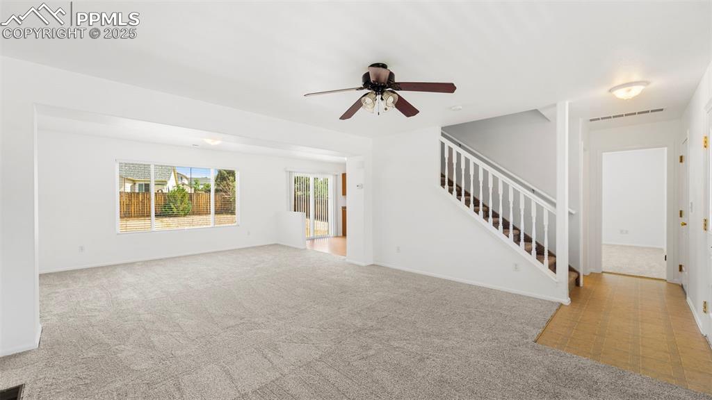 Image 8 of 46: Unfurnished living room with stairway, carpet, and ceiling fan