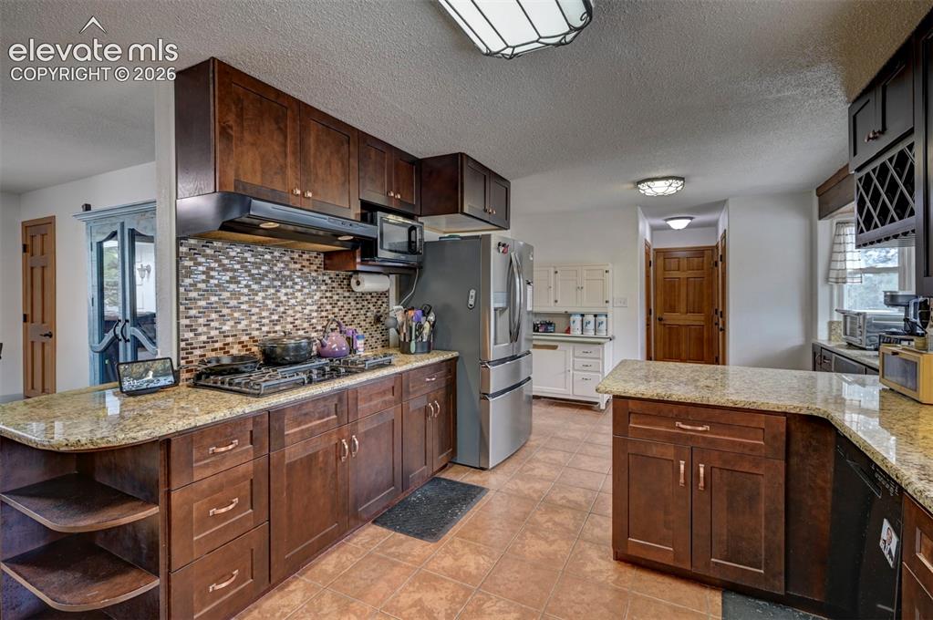 Image 11 of 50: Kitchen featuring dark wood-finish cabinetry, light speckled countertops, a