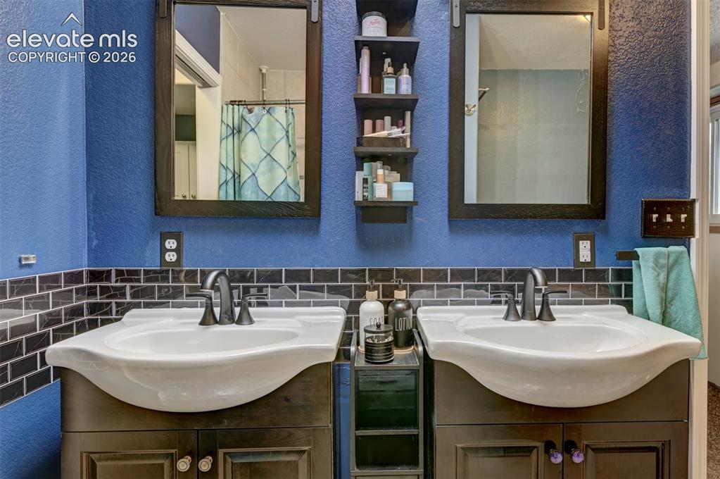 Image 16 of 50: Dual vanity with dark wood-finish cabinetry, black subway tile backsplash,