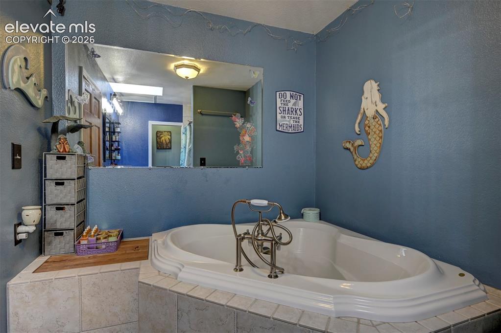 Image 17 of 50: Built-in corner soaking tub with deck-mounted faucet, surrounded by tiled p