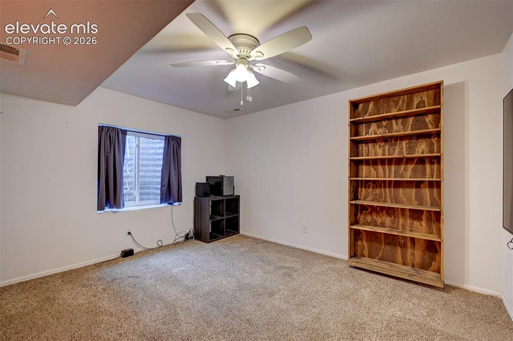 Image 31 of 50: Built-in wood shelving, textured carpeting, and a ceiling fan with integrat