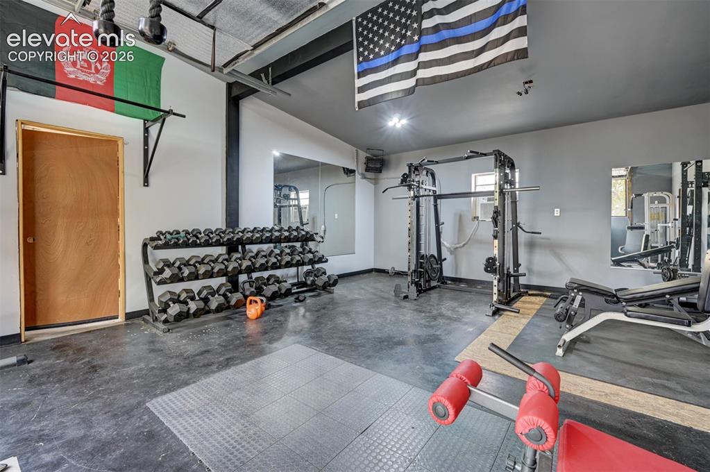 Image 35 of 50: Dedicated fitness area with concrete flooring, wall-mounted mirrors, and tr